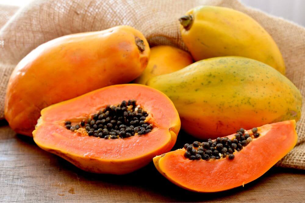 Fresh ripe papayas with seeds displayed on a rustic wooden surface, showcasing their orange flesh and black seed