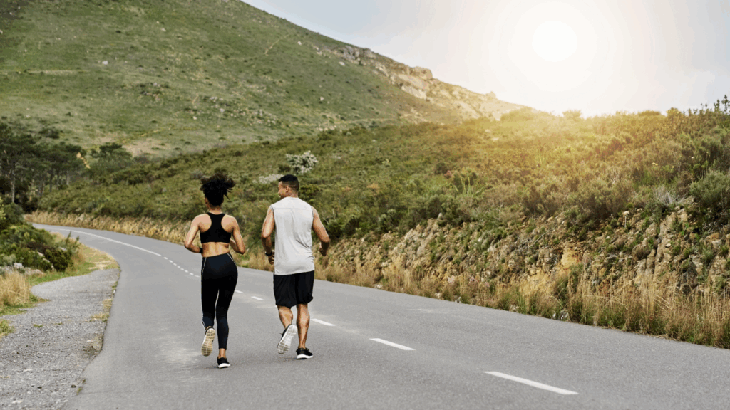 Two people a couple running on the road near the mountains.