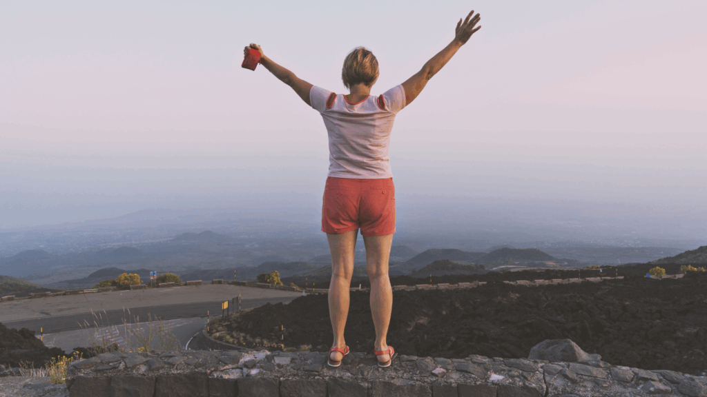 Woman in white t-shirt and red shorts in front of mountains after a hike.