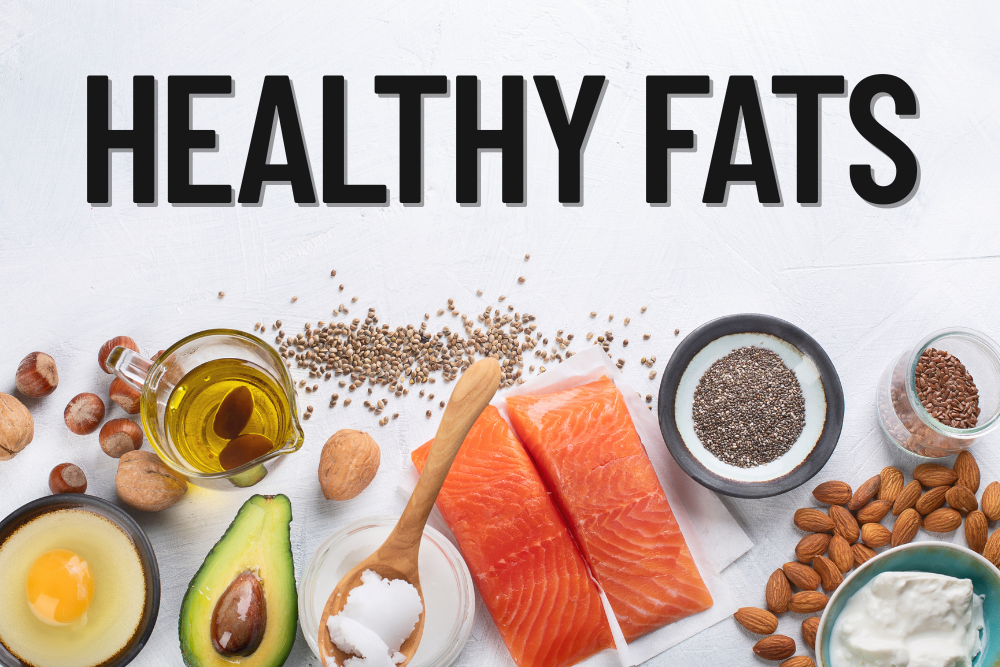 Healthy fats like salmon, avocado, nuts, seeds, and olive oil on a white background.