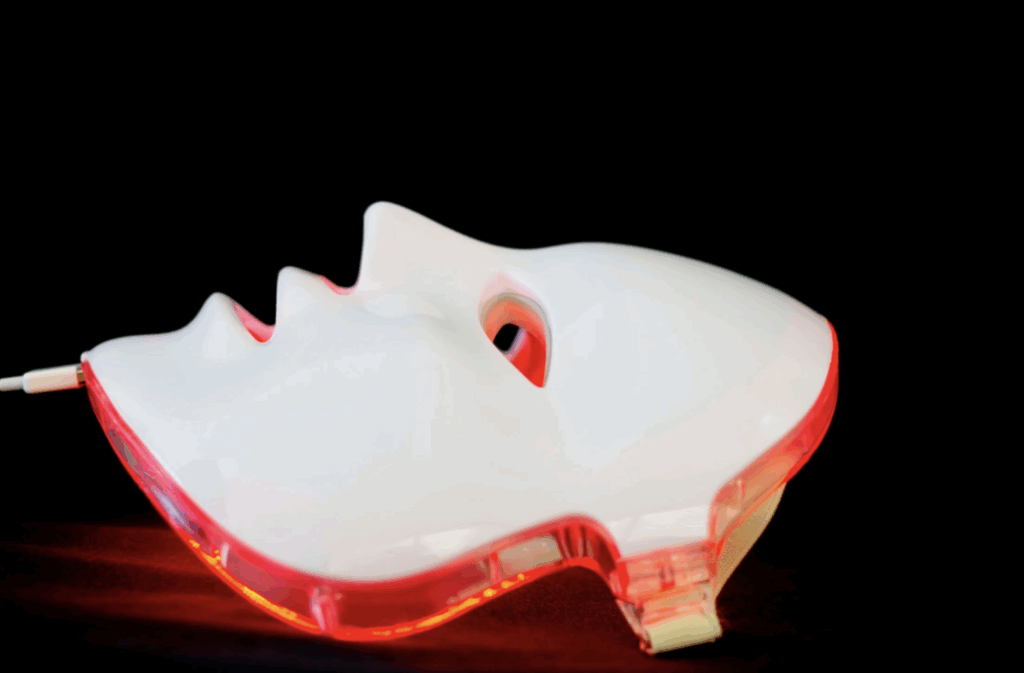 Close-up of a white LED red light therapy mask glowing with red light on a black background.